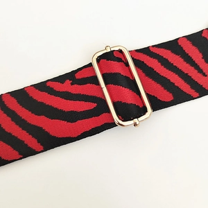 Detail of red and black zebra pattern woven strap with adjustable gold buckle