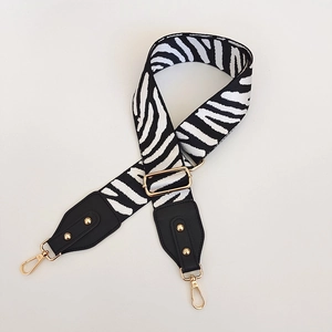 Detail of adjustable zebra print bag strap with golden metal buckles and black leather ends