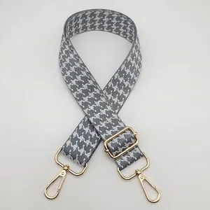 Detail of adjustable houndstooth bag strap with gold metal buckle and gray-white weave