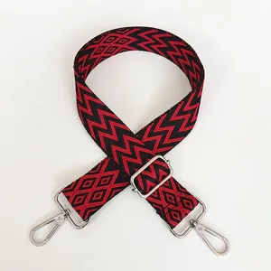 Détail de la bandoulière large tissée rouge et noir avec des mousquetons en métal argenté