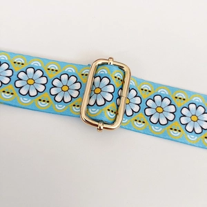 Detail of light blue ethnic floral strap with white daisy pattern and gold metal buckle