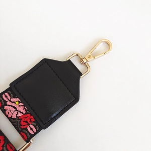 Détail de la sangle brodée de fleurs avec crochet doré et connecteur en cuir noir pour sac