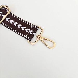 Detail of dark brown adjustable nylon bag strap with white chevron jacquard and gold metal hook