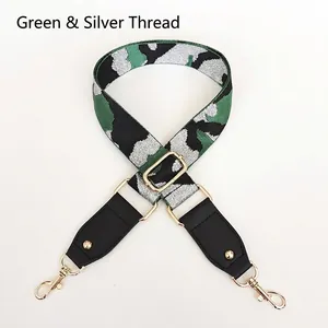 Detail view of green camo bag strap with silver thread, leather ends, and gold metal hooks