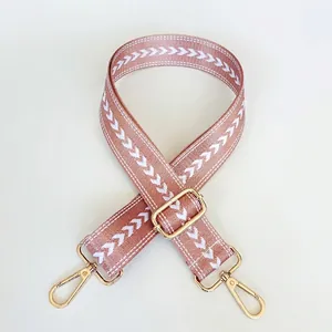 Close-up of pink nylon bag strap with white V-pattern and gold metal hardware hooks