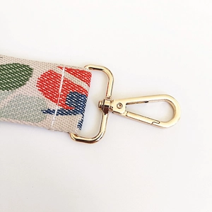 Close-up of wide canvas bag strap with colorful floral pattern and golden metal buckles