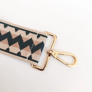 Close-up of wide woven bag strap with geometric patterns and gold lobster clasp