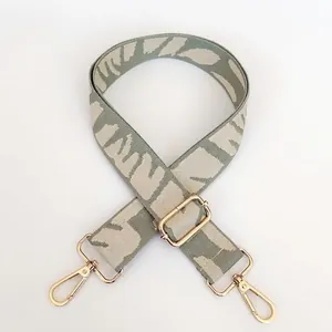 Close-up of embroidered wide bag strap in grey-green and beige with gold metal hooks