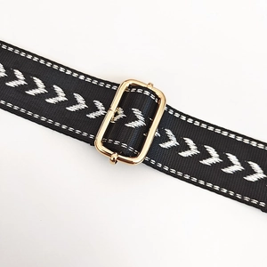 Detail of black woven strap with white arrow embroidery and polished gold metal buckle