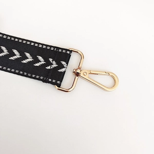 Detail of adjustable black nylon bag strap with silver V-pattern and gold metal lobster clasp