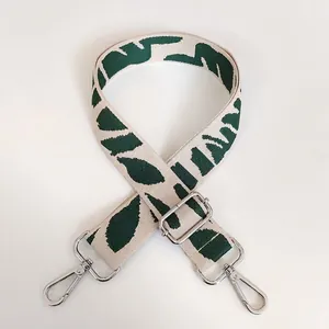 Detail view of embroidered beige bag strap with green leaf patterns and silver metal clasps
