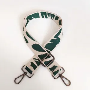 Detail of adjustable woven shoulder strap with green leaf pattern and dark metal hooks