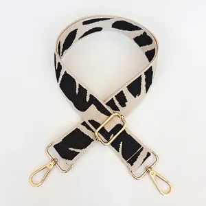 Close-up of black and white patterned wide woven shoulder strap with gold metal hooks