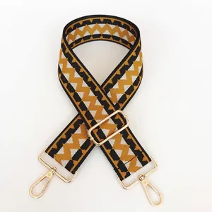 Detail view of ethnic style wide woven bag strap with geometric patterns and gold buckles