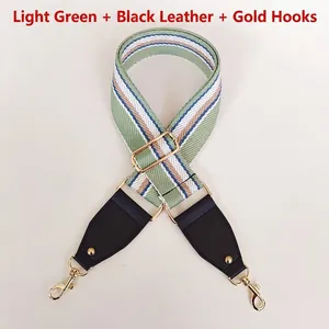 Detail of light green striped canvas bag strap with black leather and gold metal hooks