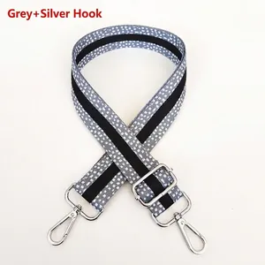 Detail of adjustable grey spotted fabric bag strap with silver metal hooks and buckle