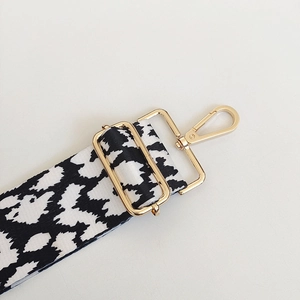 Detail of adjustable black and white cow print strap with premium gold metal hardware