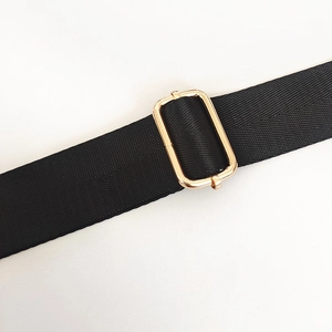 Macro detail of thick black nylon shoulder strap with a shiny gold adjustable metal buckle