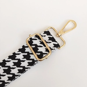 Close-up of black and white houndstooth jacquard bag strap with gold metal lobster clasp