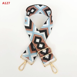 Detail of wide jacquard bag strap with geometric rhombus pattern and gold metal hooks