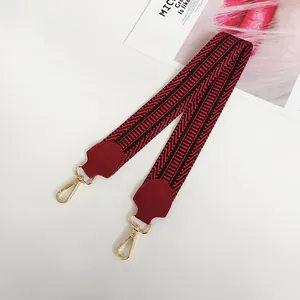Macro shot of burgundy wide canvas bag strap with gold metal hooks and geometric patterns