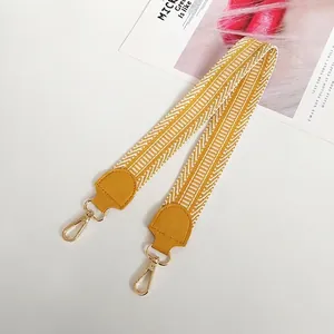 Close-up of a wide woven bag strap with yellow geometric patterns and gold metal hook