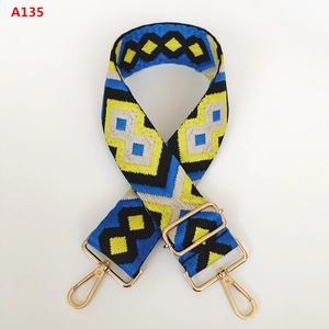 Detail of wide woven bag strap with geometric diamond pattern and golden metal hooks