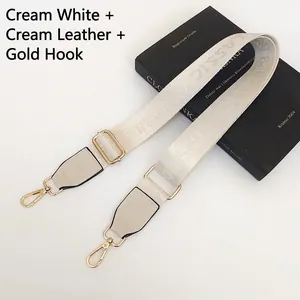 Detail of cream white nylon bag strap with gold hooks and leather trim on a black book