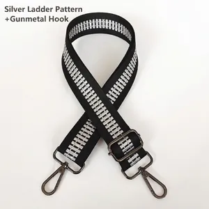 Detailed view of wide black crossbody bag strap with silver pattern and gunmetal hooks