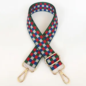 Détail d'une bandoulière tissée ajustable avec motif damier vert, rouge et bleu et crochets dorés
