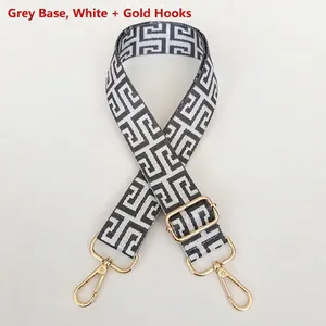 Detail of adjustable bag strap featuring grey and white Greek key pattern with gold hooks