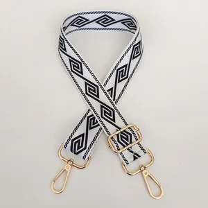 Detail view of white geometric strap with black Greek patterns and gold swivel hooks