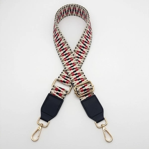 Detail of adjustable woven shoulder strap with red geometric patterns and gold metal buckles