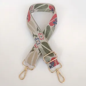 Detailed macro view of beige jacquard bag strap with floral pattern and golden metal hook