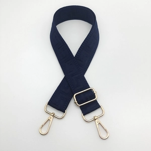Detail of navy blue wide canvas bag strap with geometric texture and gold metal hooks