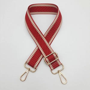 Détail de la bandoulière tressée rouge et blanche avec mousquetons dorés en métal