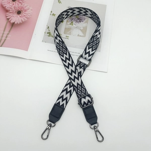 Detail of adjustable black and white embroidered bag strap with metal hooks and gear pattern