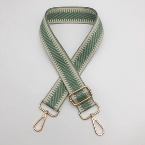 Détail de la bandoulière tissée vert et beige avec mousquetons métalliques dorés