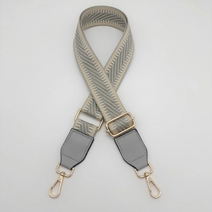 Detail of adjustable grey herringbone bag strap with golden metal hardware and leather ends