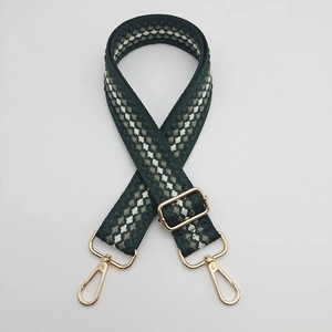 Detail of adjustable woven bag strap with green pattern and gold metal buckles