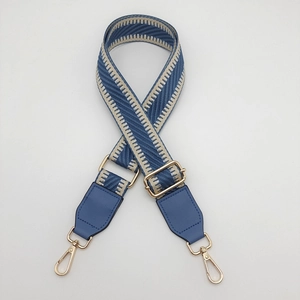 Detail of adjustable blue and beige herringbone woven bag strap with gold metal hardware