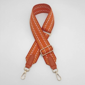 Close-up of orange geometric woven bag strap with golden metal hooks and leather ends