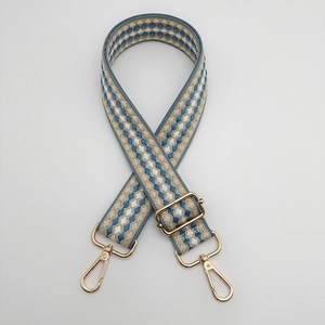 Close-up of adjustable blue and beige checkered woven bag strap with gold metal buckles