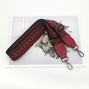 Detail view of adjustable woven bag strap with red leather ends and metal hooks