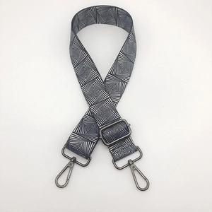 Detail of wide nylon bag strap with black and white geometric swirl pattern and metal hooks