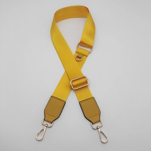 Detail view of bright yellow nylon bag strap with gold metal hooks and adjustable buckle