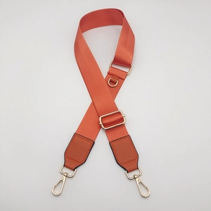 Close-up of orange nylon bag strap featuring gold metal hooks and durable D-ring buckle