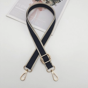 Detail of adjustable wide shoulder strap featuring black and white geometric pattern and gold buckle