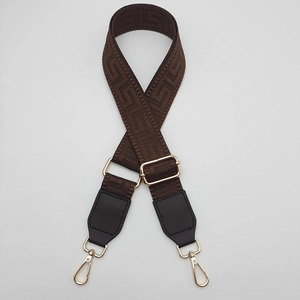 Close-up of wide geometric pattern bag strap with brown leather and gold metal buckles