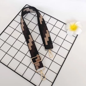 Close-up of wide geometric jacquard bag strap with gold metal buckles on a grid